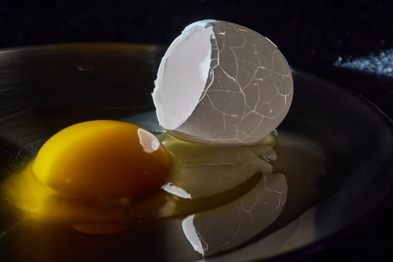 A delicate, cracked eggshell floats on a dark, reflective surface, its translucent form glowing softly in the dim light